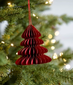 Detail of red honeycomb paper Christmas tree ornament hanging on a green branch with bokeh
