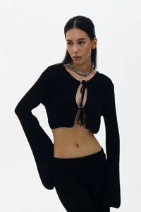 Détail d'un cardigan court en maille noire avec lacets sur le devant et manches évasées