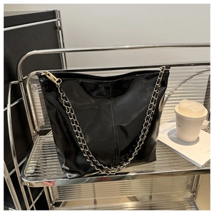 Detail of a black glossy shoulder bag featuring a stylish gold chain strap on a metal shelf