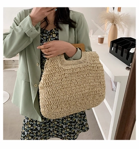 Close-up of a large beige woven straw tote bag with square wooden handles on a model