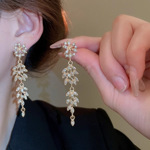 Détail des boucles d'oreilles dorées à glands avec strass et motif de feuilles