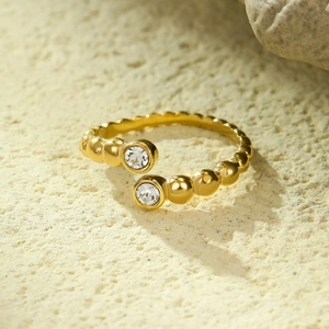 Detailed view of a gold beaded open ring with round zircon studs on a textured stone base