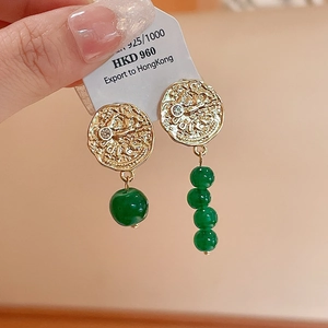 Détail de boucles d'oreilles en argent 925 avec reliefs dorés et perles vertes en main