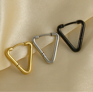 Tre orecchini a triangolo in titanio nei colori oro, argento e nero su raso beige