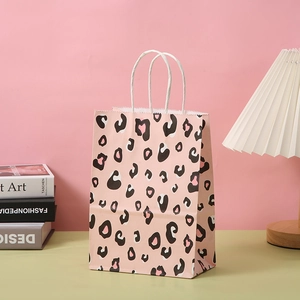 Pink leopard print paper gift bag with white twisted handles on a stylish desktop