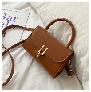 Close-up of brown leather crossbody bag with metal turn-lock and adjustable strap