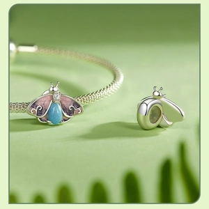 Macro detail of S925 silver moth bead with pink enamel wings and blue gemstone inlay