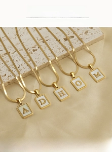 Detail of square shell initial pendants in gold plating on a premium satin background