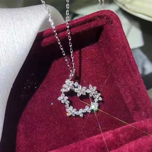 Makroaufnahme vom silbernen herzförmigen Blumenanhänger mit Zirkonia auf rotem Samt