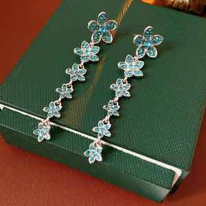 Détail macro de boucles d'oreilles à pompons argentés avec fleurs en zircon bleu sur boîte