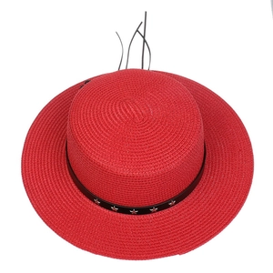 Close-up of a red straw sun hat featuring a black band with silver star rivets and feathers