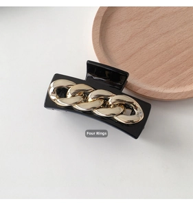 Detail of a large black claw clip with four decorative gold chain links on a wooden tray