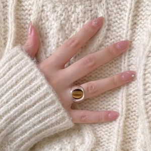 Close-up of tiger eye stone silver ring worn with a beige knitted sweater background