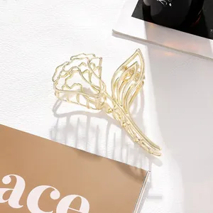 Detailed close-up of a gold metal rose hair claw clip with hollow floral and leaf design