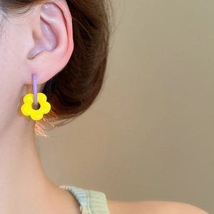 Close-up of vibrant purple hoop earrings with yellow flower pendants on model ear