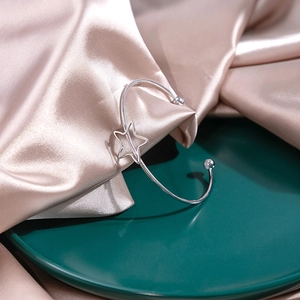 Detail shot of silver open bangle with star charm and bead ends on satin fabric