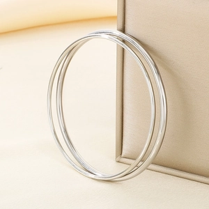 Close-up of two polished silver round bangles leaning against a textured beige gift box