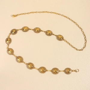 Golden metal chain belt with oval engraved discs and lobster clasp on beige surface