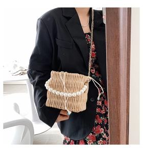 Detail of hand-woven straw bucket bag with large pearl handle and golden chain strap