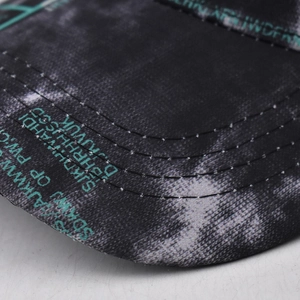 Detailed close-up of teal typography print on black tie-dye baseball cap brim