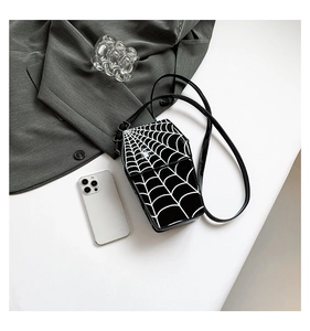 Flat lay of coffin-shaped spider web crossbody bag with phone and grey blazer on white background