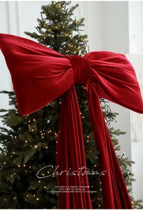 Close-up of giant burgundy velvet Christmas bow with long ribbons on a lighted tree
