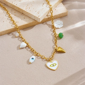 Goldkette mit Evil Eye Herzanhänger und Muschelcharms auf einer Steinplatte
