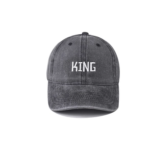 Detailed close-up of white KING embroidery on washed dark grey baseball cap cotton fabric