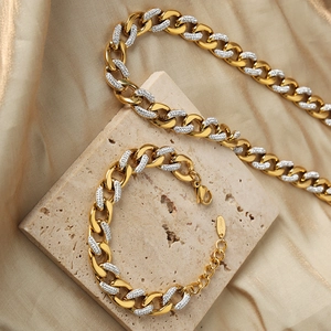 Polished two-tone gold and silver Cuban link necklace and bracelet set on stone base