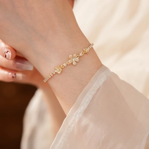 Dettaglio di un elegante bracciale a fiori dorati con zirconi lucenti indossato al polso