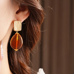 Close-up of model wearing gold square metal studs with amber resin teardrop earrings
