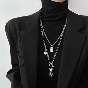 Detail of layered silver necklaces with teddy bear pendant and rectangle tag on black suit