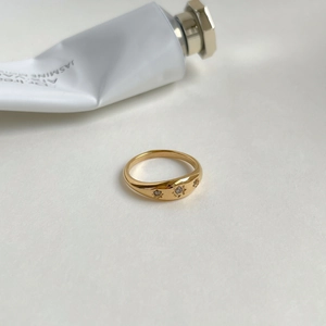 Detail of gold-plated signet ring with three star-set zircons on warm white background