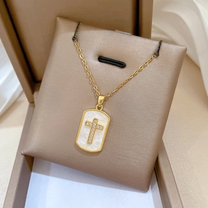 Detailed view of a gold shell cross necklace with crystals in a beige velvet jewelry box
