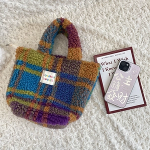 Close-up of colorful checkered faux shearling handbag with brand label on soft white rug