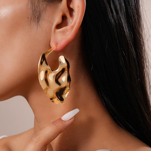 Détail d'une femme portant une boucle d'oreille dorée ondulée à finition polie