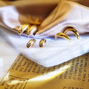 Teardrop and C-shape gold earrings displayed on elegant champagne silk and newspaper