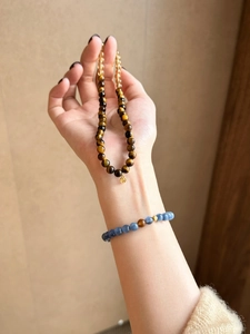 Detailed view of layered tiger eye and blue quartz beaded bracelets with gold charms