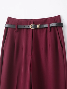 Detailed close-up of high-waisted burgundy trousers featuring a black belt with gold buckle