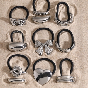Polished silver metal hair ties with various geometric designs on sand background