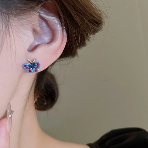Close-up of model wearing blue and red butterfly stud earrings with gold plating