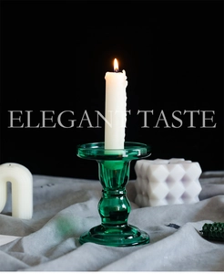 Detail of green glass candle holder with elegant white pillar candle on dark base