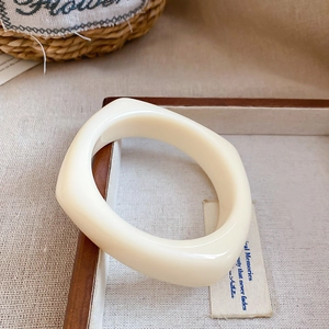 Close-up of a glossy cream acrylic geometric square bangle on a rustic wooden tray