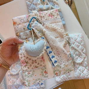 Close-up of quilted floral bag with heart pendant, pearl handle, and lace detail