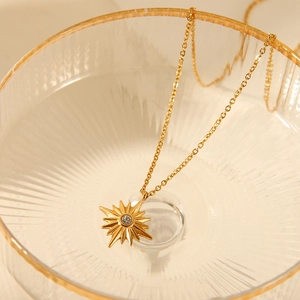 Close-up of golden sunburst pendant necklace with clear crystal in textured glass dish