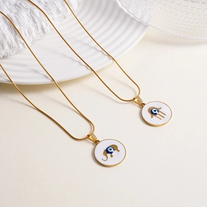 Gold Hamsa Hand and Elephant necklaces with white enamel evil eye pendants on ceramic