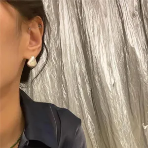 Close-up of silver shell-shaped earrings and minimalist studs on a female ear model