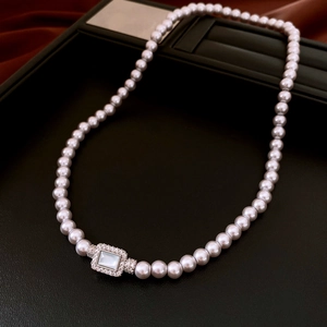 Close-up of grey-pink pearls with a rectangular zircon clasp on a black leather tray