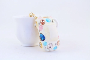 Detail of white car-shaped keychain with colorful rhinestones leaning on a tea cup