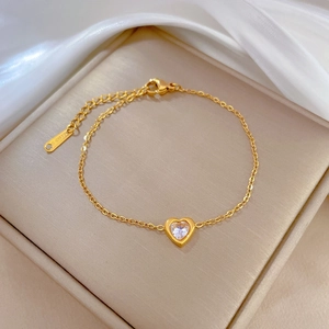Detail of gold heart zircon bracelet resting on elegant champagne silk inside a jewelry box